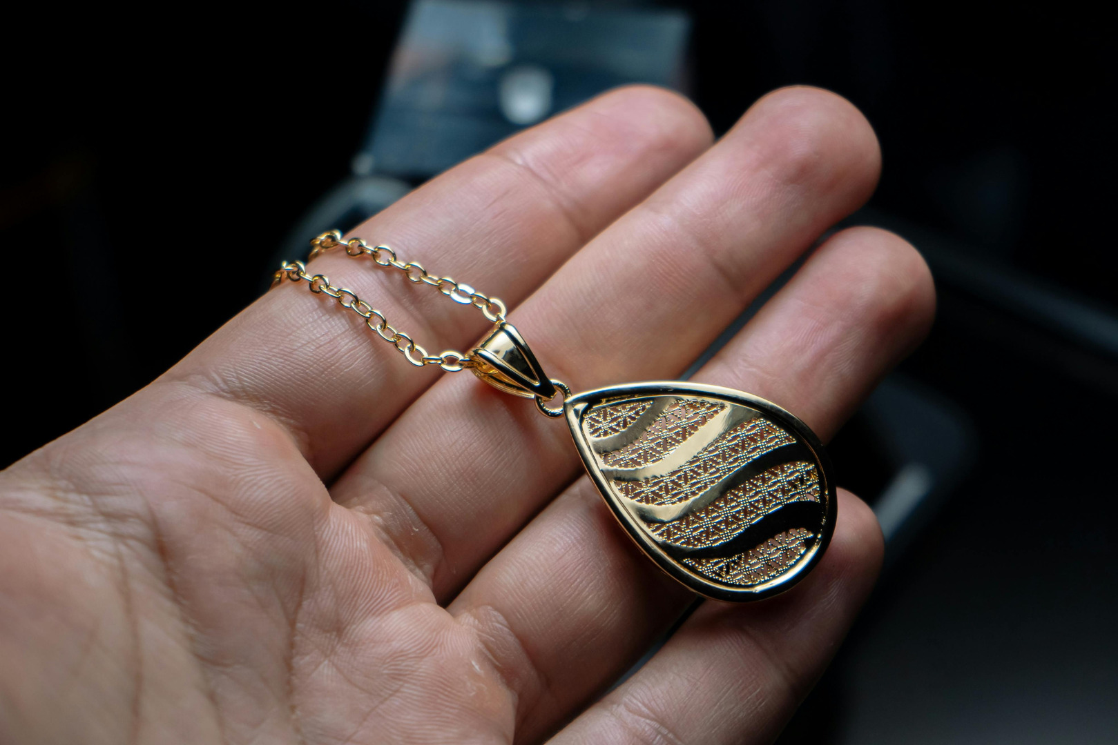 Hand holding a detailed gold necklace pendant with intricate design.