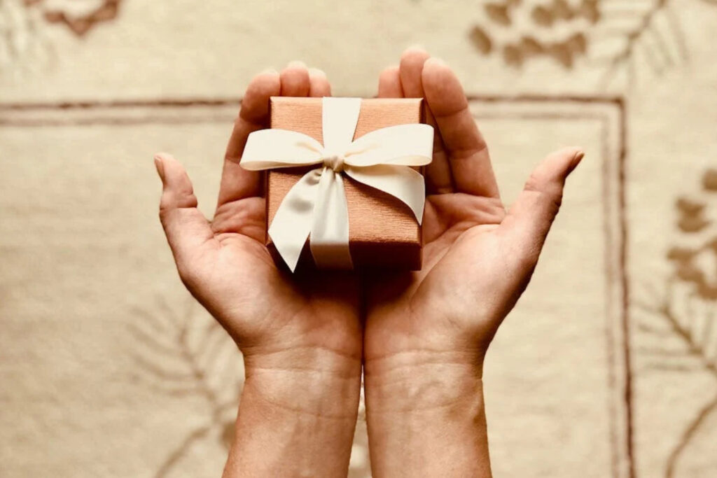 Hands holding a wrapped gift box with ribbon - Jewelry Gift Ideas for the holidays