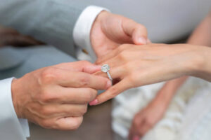 Close-up of a groom placing a ring on his bride’s hand to get a new engagement ring look