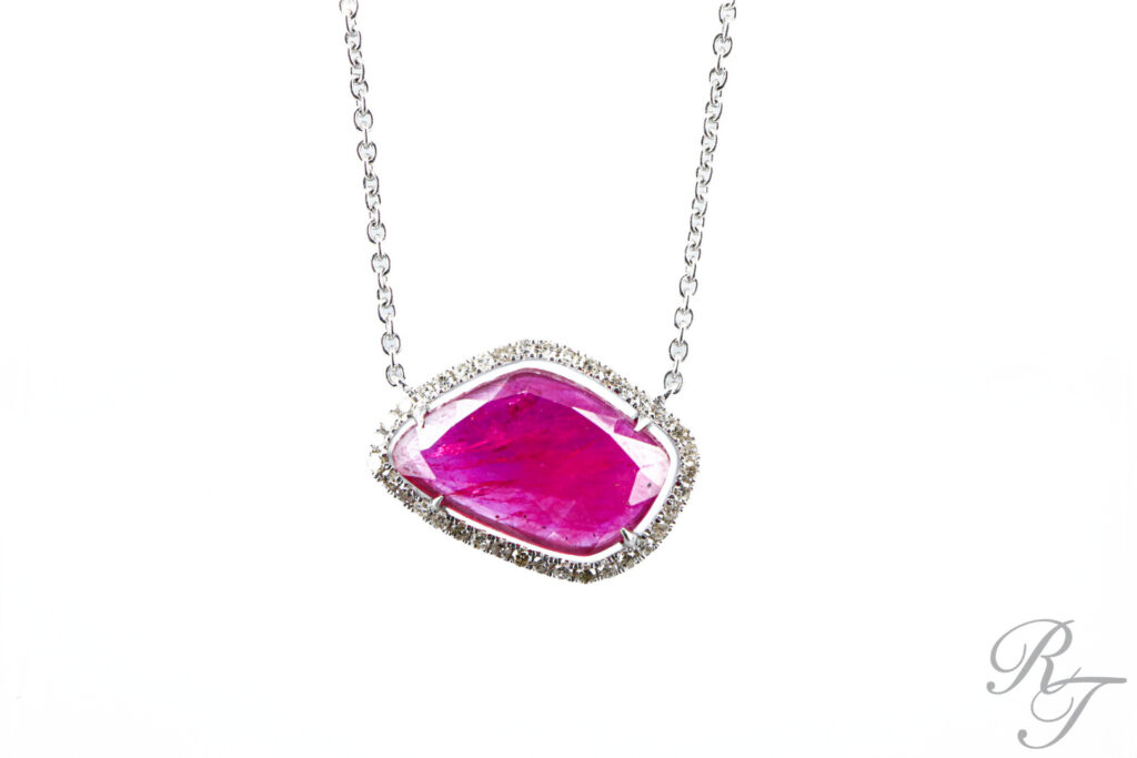 A custom necklace featuring a large, unique-cut pink gemstone surrounded by a diamond halo on a white gold chain.