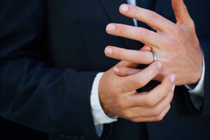 A man in a suit adjusts a simple, custom wedding band on his finger, showcasing one of the most popular Custom Jewelry Ideas for Men.