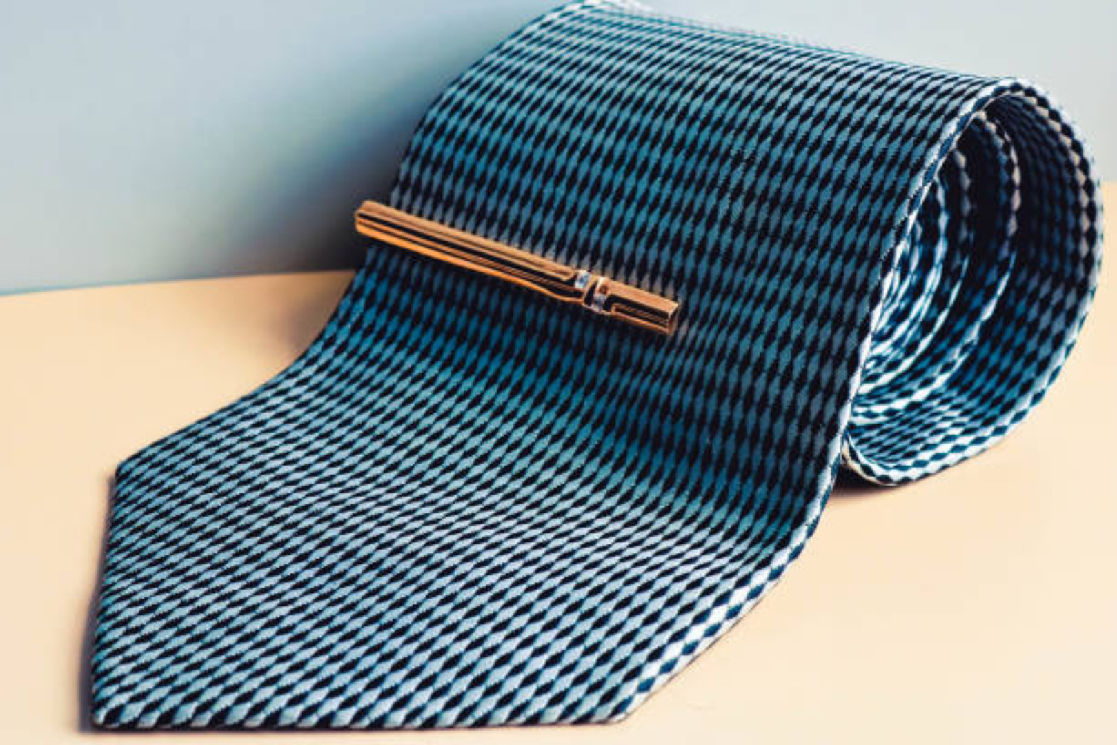 A stylish gold tie clip on a blue patterned tie, representing a sophisticated accessory from our list of Custom Jewelry Ideas for Men.