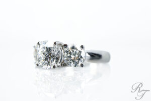 A side-view of a three-stone diamond ring, showing the secure prongs and tips holding each round brilliant diamond in place.