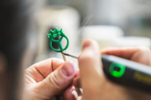 A close-up of a jeweler using a tool to refine a green wax mold for a custom ring setting, showing the first step in creating a Gemstone for Your Zodiac piece.