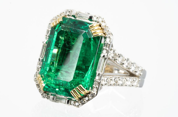 A custom engagement ring featuring a large, vibrant emerald gemstone surrounded by a diamond halo, a powerful Gemstone for Your Zodiac sign.