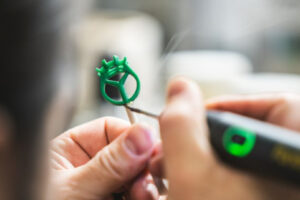 A close-up of a jeweler using a tool to shape the green wax mold for a custom engagement ring setting.