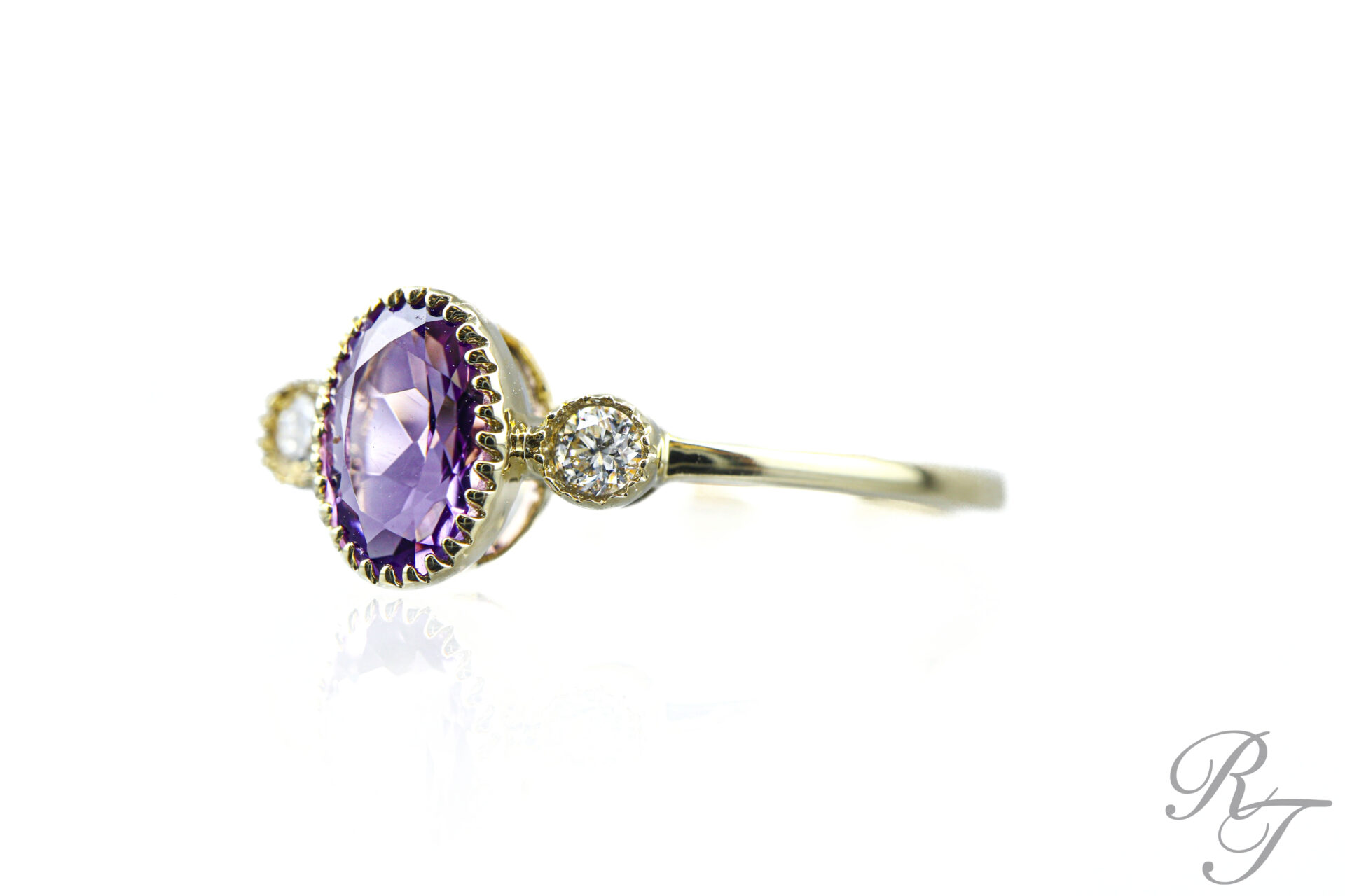 Close-up profile view of a custom three-stone gold ring featuring an oval purple gemstone in a scalloped bezel setting flanked by two round diamonds.
