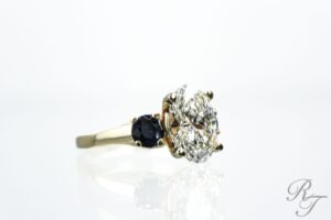 Side profile of an oval diamond engagement ring with a six-prong setting and blue sapphire side stones, illustrating healthy, secure prongs from Rick Terry Jewelry Designs.