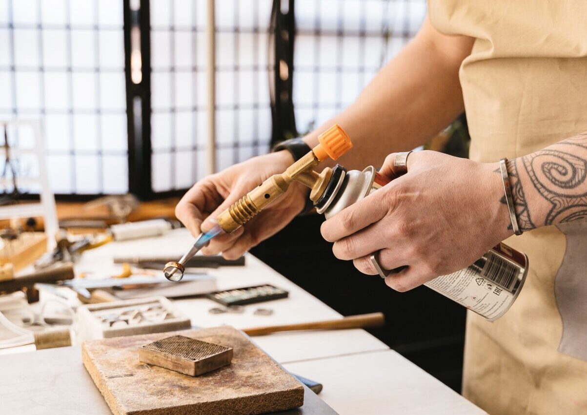 Jeweler using a blowtorch to solder a metal ring at a jewelry workbench with professional tools