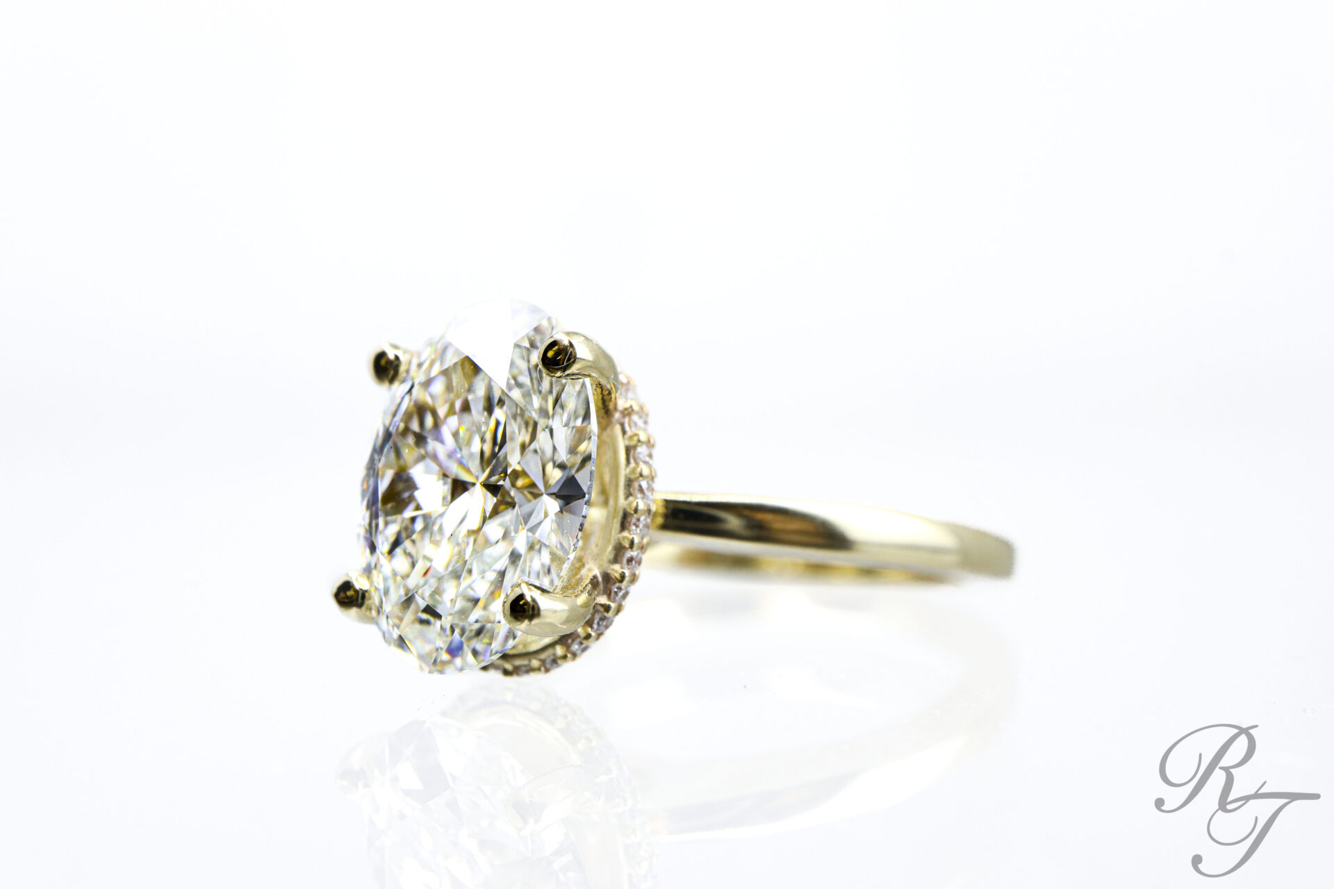 Oval diamond engagement ring in a four-prong yellow gold setting with hidden halo designed by Rick Terry Jewelry in Knoxville TN