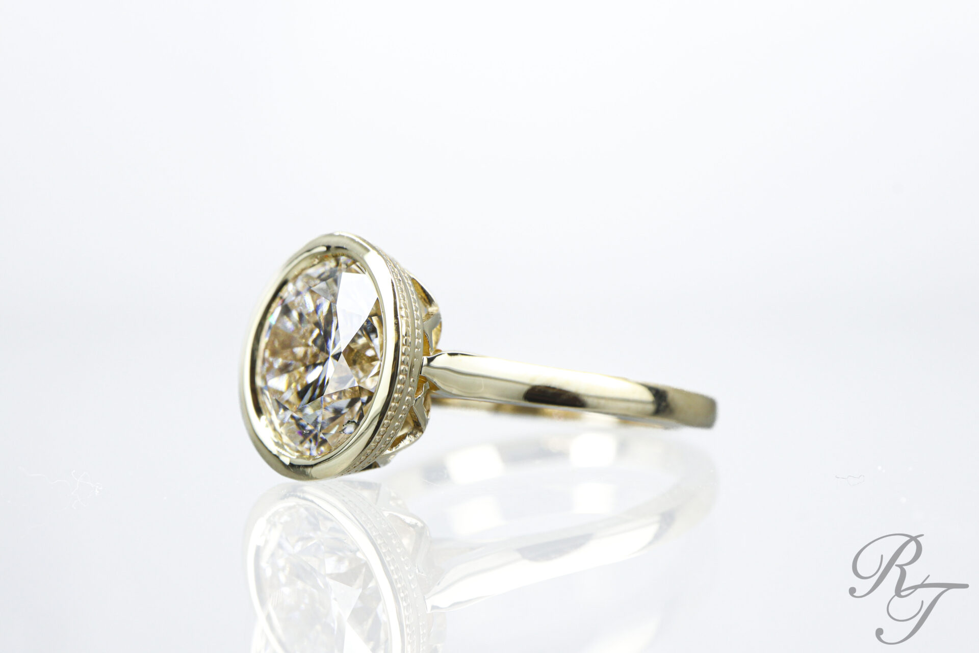 Custom oval diamond bezel setting engagement ring in yellow gold with milgrain detail by Rick Terry Jewelry Designs Knoxville