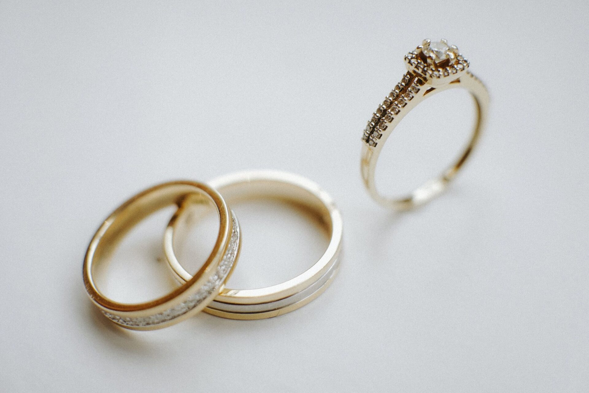 Gold engagement ring with halo setting alongside matching wedding bands on a neutral background